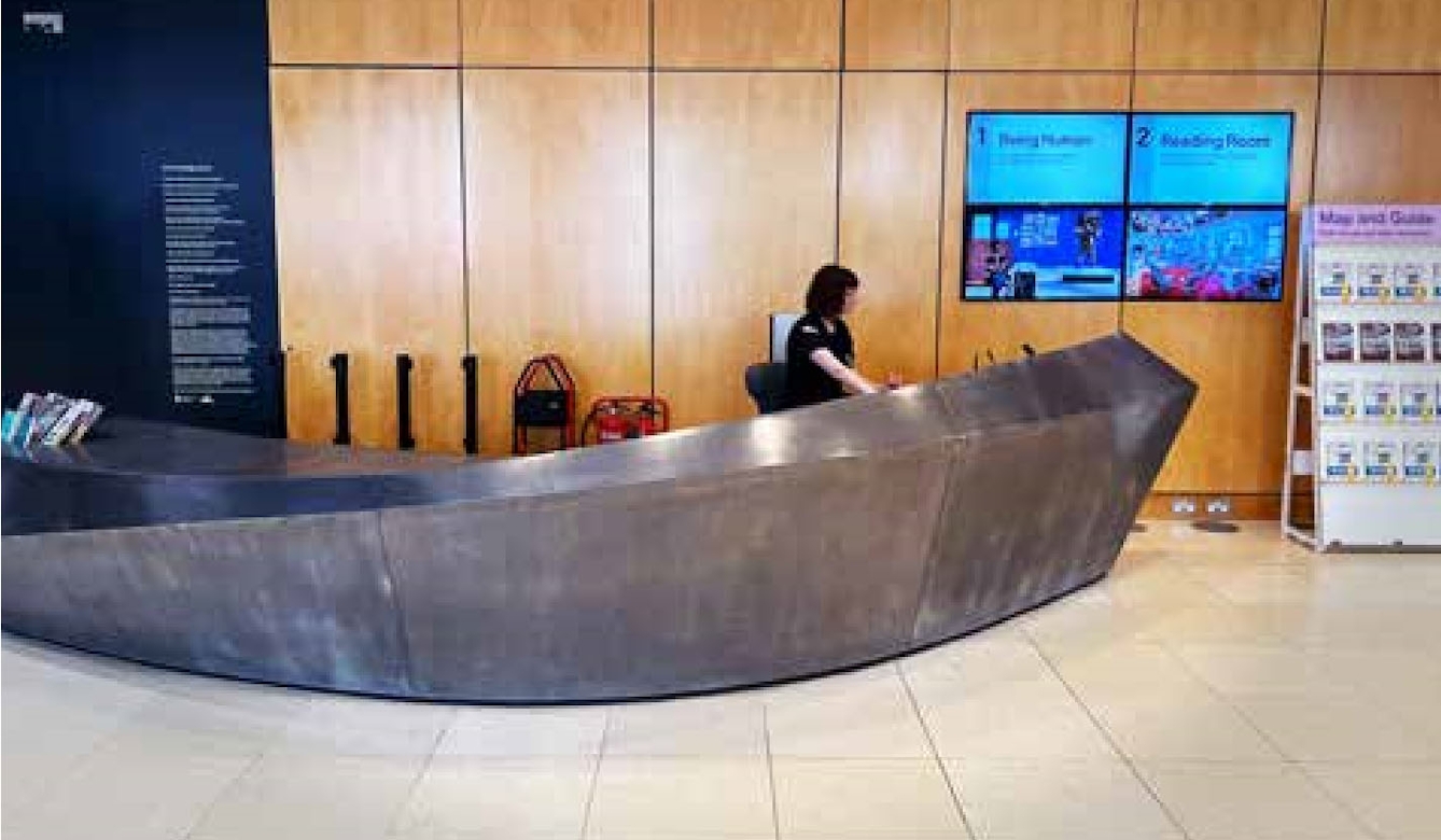 A long sweeping metal structure forms a contemporary information desk in the reception area of a museum.
