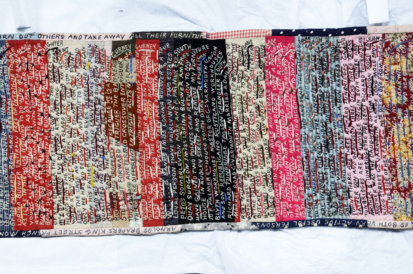 Colour photograph of an embroidered patchwork scroll in various colours stitched together and covered with words in capital letters. The stitching includes words such as "Miss Lorina Bulwer am a true loyal person".