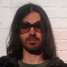 Head and shoulders photograph of a man with glasses, a beard and shoulder-length dark hair.