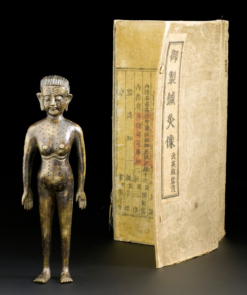 Image of bronze acupuncture figure next to scroll with Chinese text