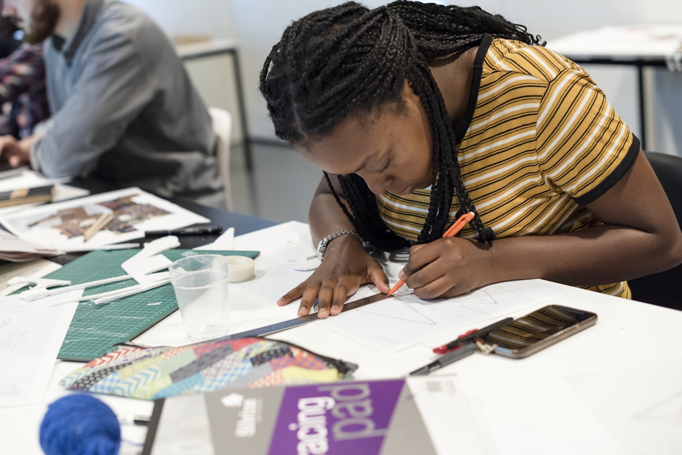 A young person sketching at a table using a ruler, pencil and paper