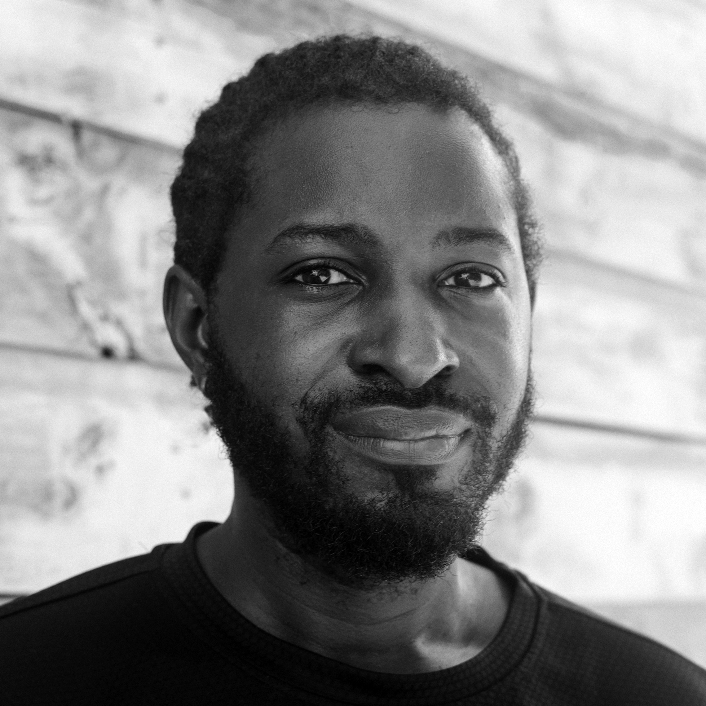 Head and shoulders photograph of a man with short hair and a beard, wearing a black crew-neck top.  