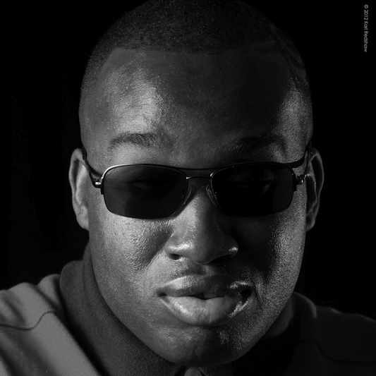 Photograph of the face of a man wearing dark glasses.