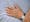 Photograph of the hands of a patient with light pink painted fingernails, resting on a light blue hospital bedsheet.
