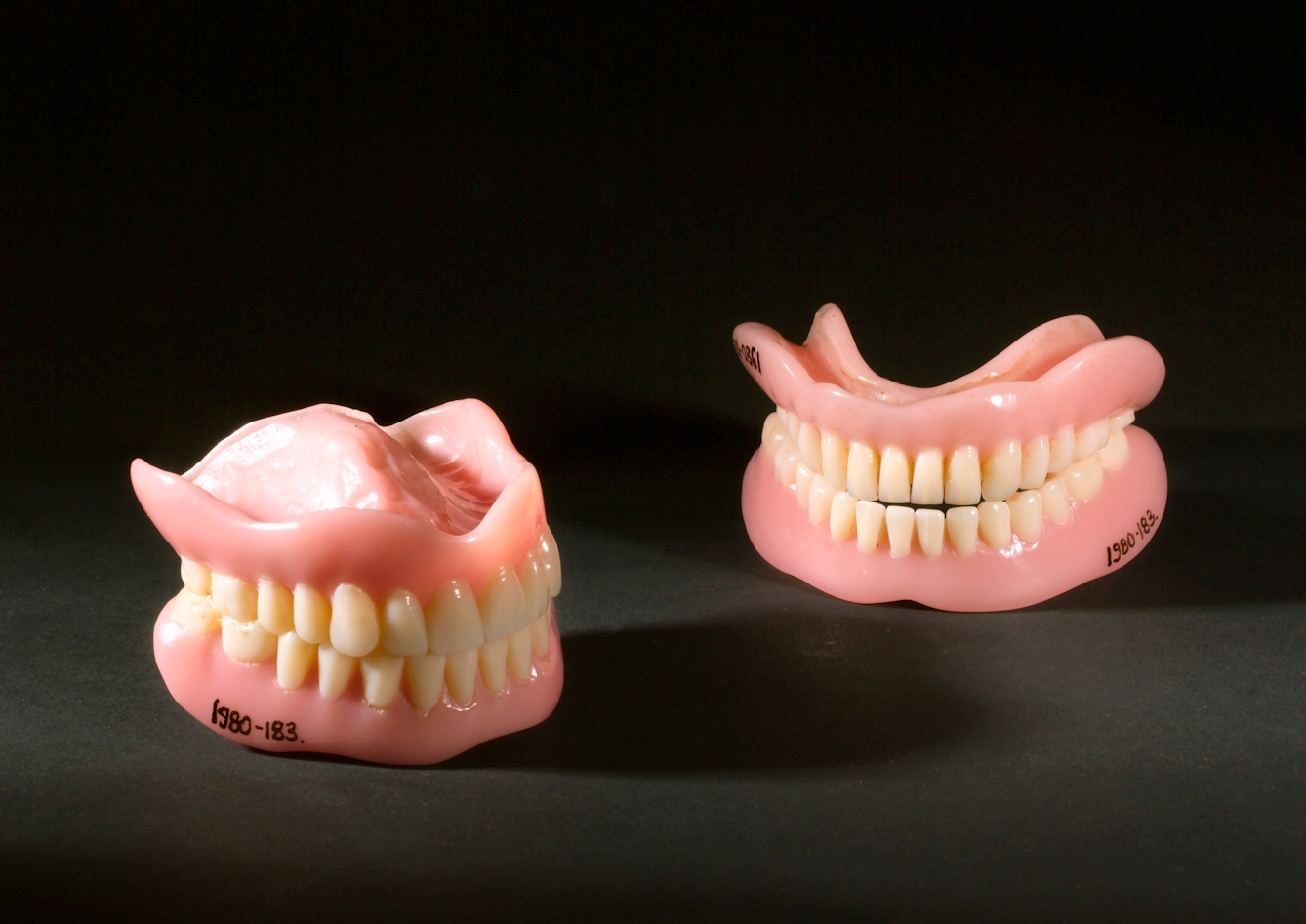 Two pairs of acrylic dentures with top and bottom teeth. Photographed on a black background.