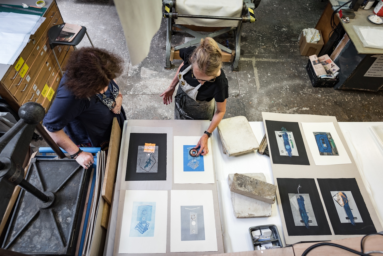 Photograph of two women in a printmaking studio, discussing the next steps in creating an printed artwork. 