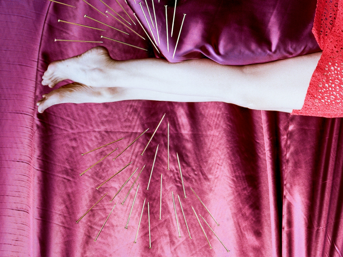 Detail from a larger artwork created with a colour photographic print of a female figure in a bright red dress, set against a purple and blue draped silk background. She is lying horizontally in the frame, face down, caught as if in mid fall. Her body is surrounded by groups of dress pins, laid on top of the photographic print. The pins are arranged as if they are a flight of arrows directed at her body. One group attacks her legs from underneath, another from above.