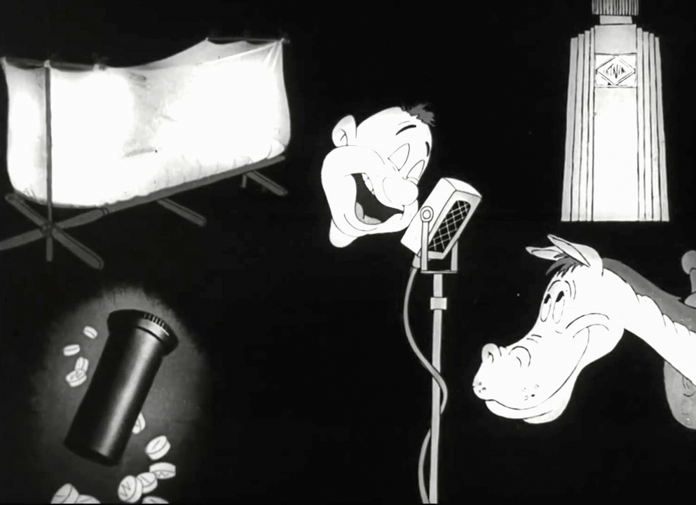 Black and white still image from the film 'Private SNAFU vs. Malaria Mike', showing Snafu's disembodied head speaking into a microphone in the centre.  In the top left is a bed with a mosquito net around it.  In the top right is a medicine bottle.  In the bottom left is a medicine bottle and pills.  In the bottom right is the head of a horse, looking up at Snafu.