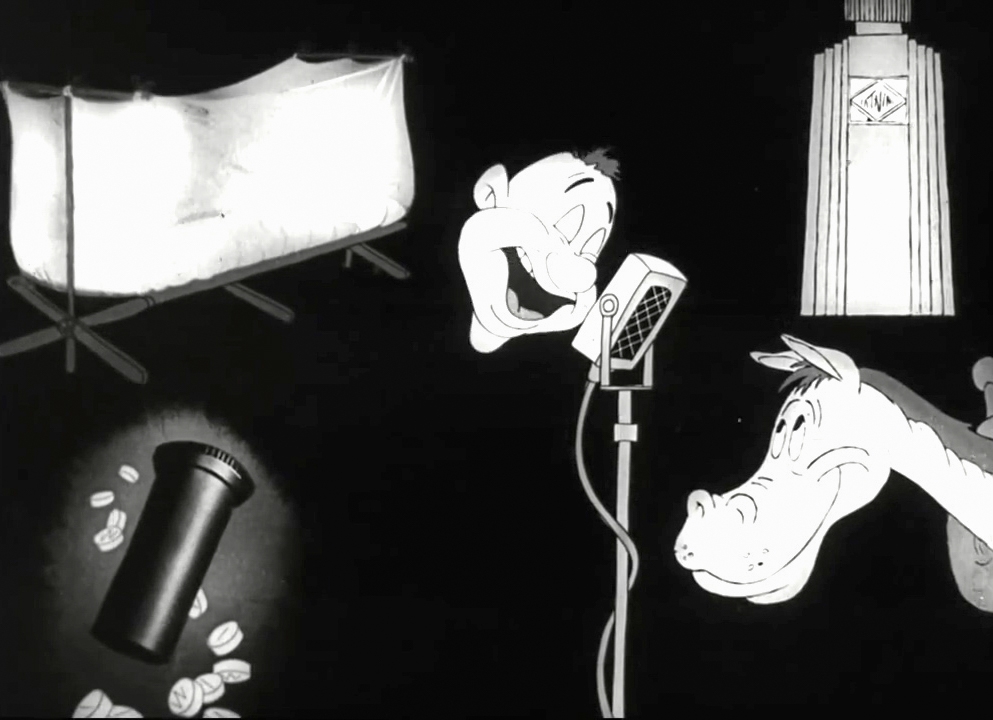 Black and white still image from the film 'Private SNAFU vs. Malaria Mike', showing Snafu's disembodied head speaking into a microphone in the centre. In the top left is a bed with a mosquito net around it. In the top right is a medicine bottle. In the bottom left is a medicine bottle and pills. In the bottom right is the head of a horse, looking up at Snafu.