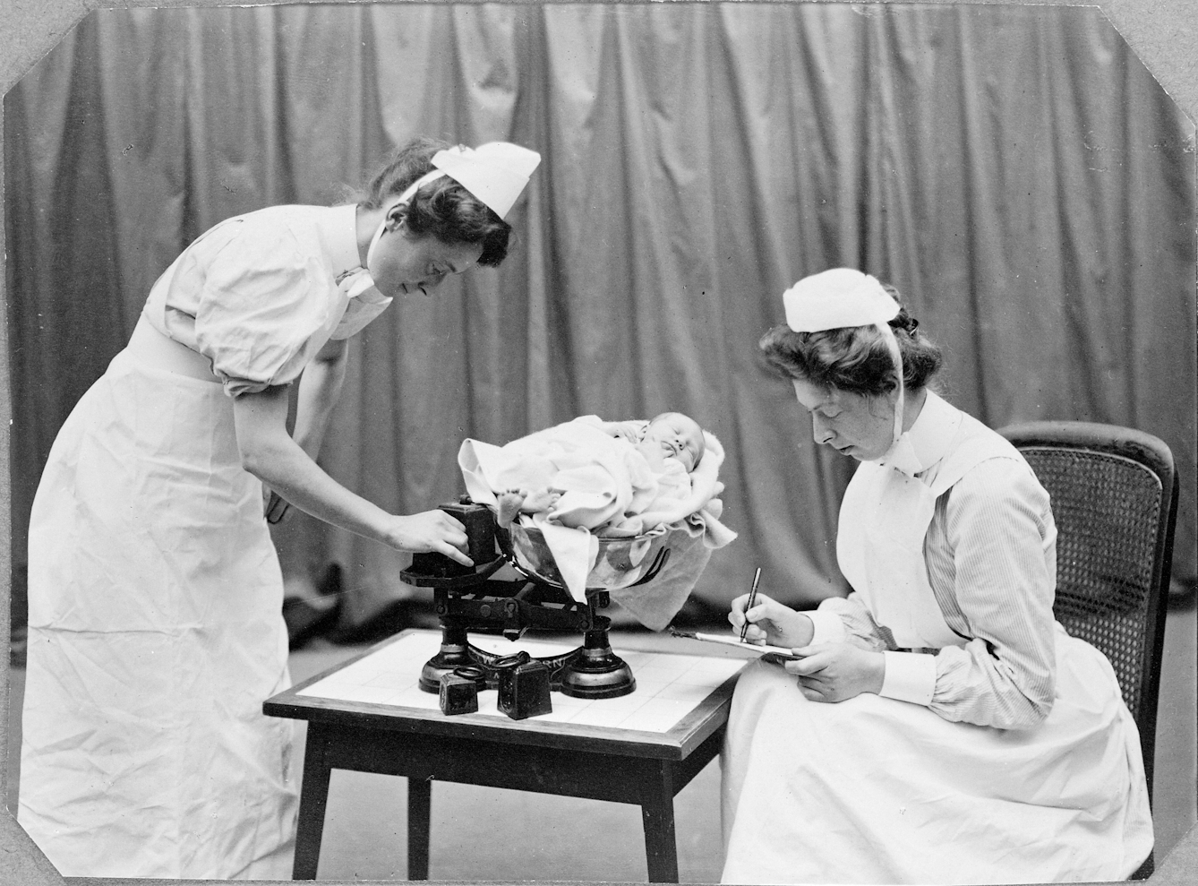 Black-and-white photograph of nurses weighing a baby at the General Lying In Hospital, York Road, Lambeth. 