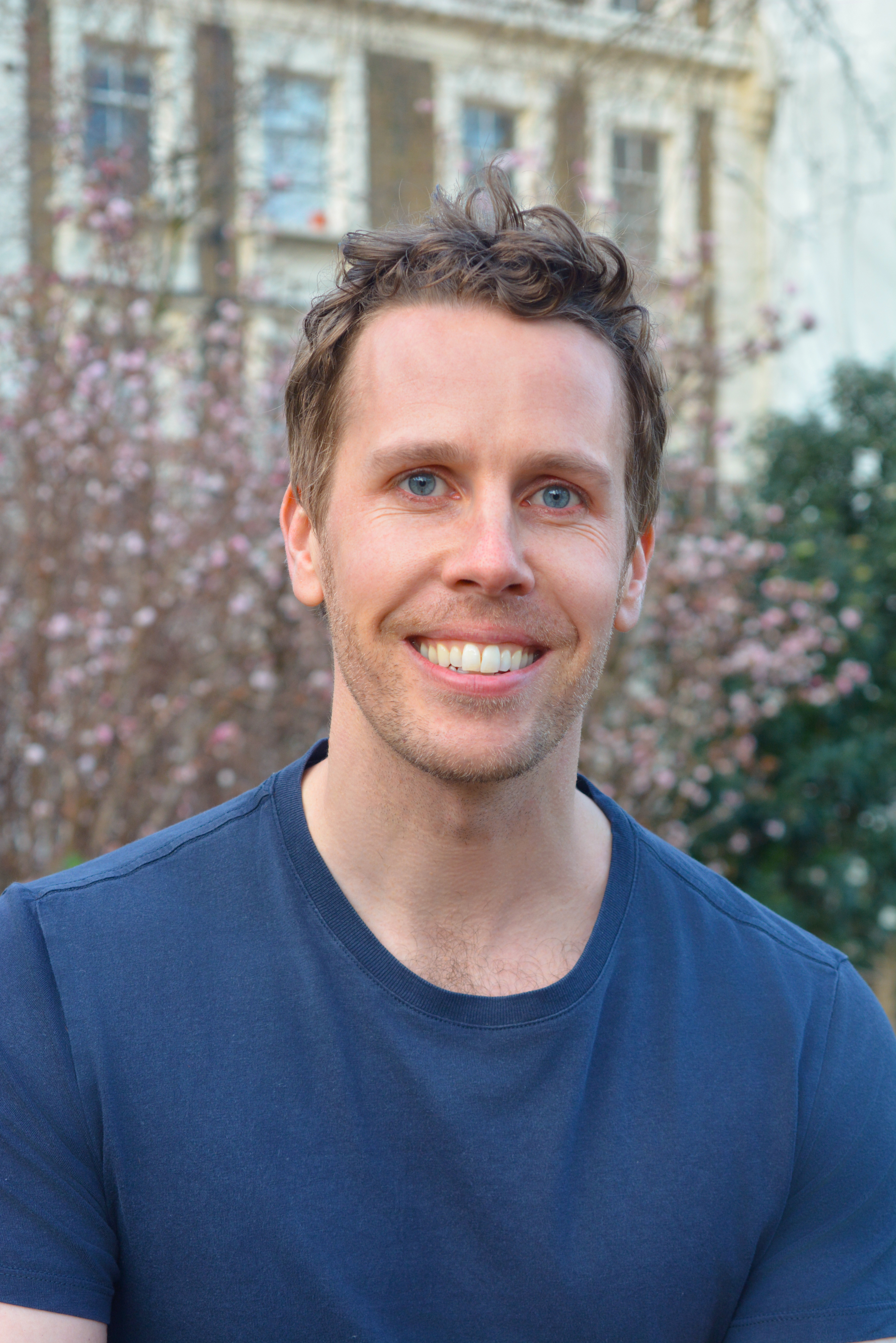 Headshot of James Muldoon wearing a blue tshirt, smiling into the camera