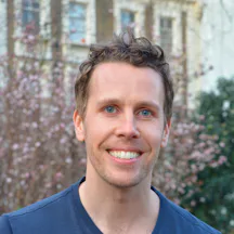 Headshot of James Muldoon wearing a blue tshirt, smiling into the camera