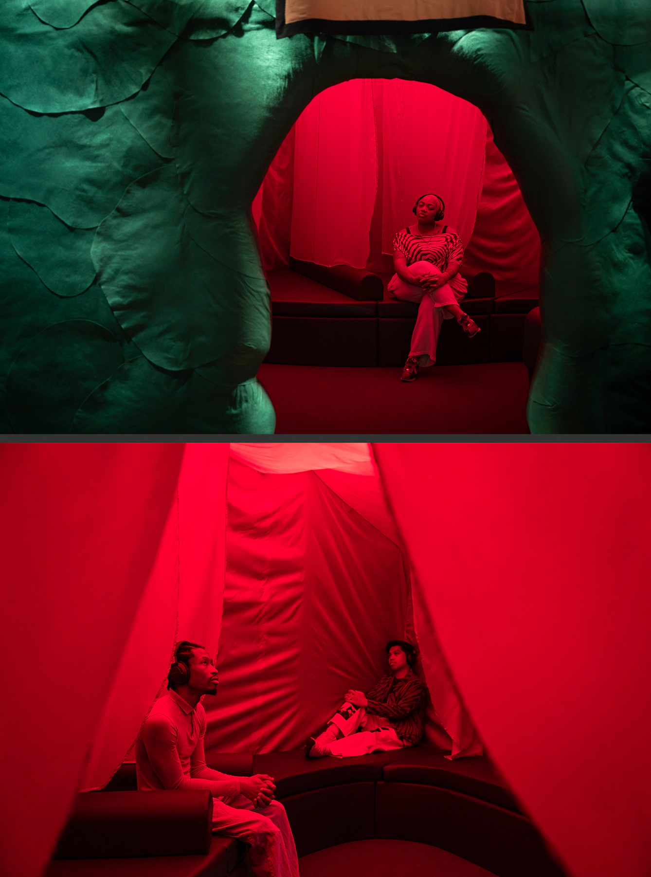 Visitors wearing headphones sit inside a red-lit sculptural installation, surrounded by draped fabric and curved seating.