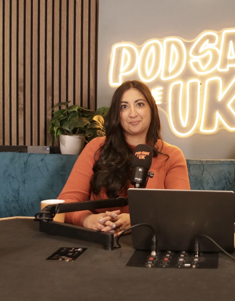 Headshot of Coco Khan sitting behind podcasting equipment 