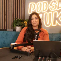 Headshot of Coco Khan sitting behind podcasting equipment