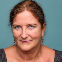 A close-up portrait of Alison Claire France looking straight to camera with a warm open gaze. The blue of her eyes compliments the blue coloured background.