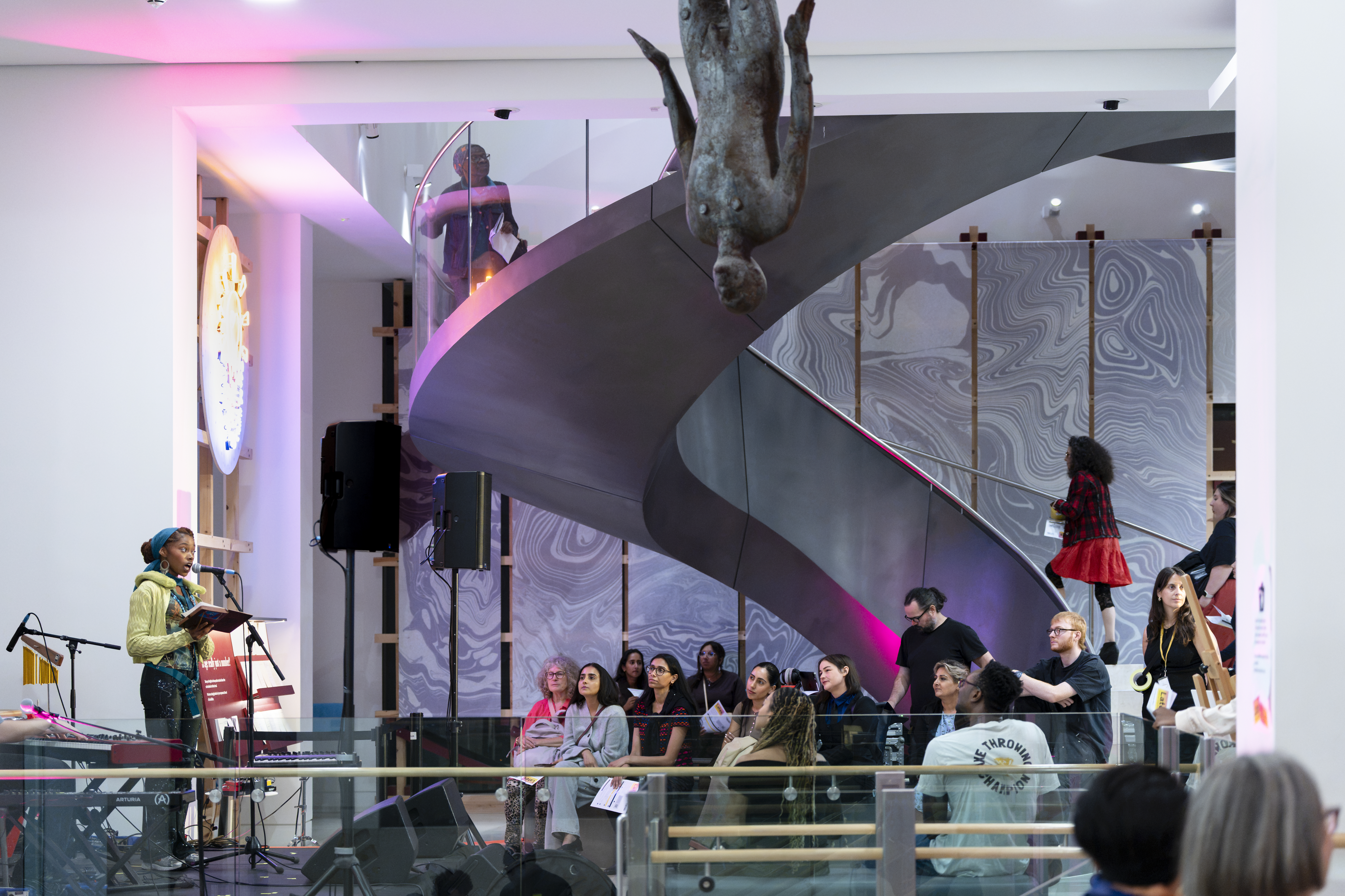 An audience watch a performer on a stage, speaking into a microphone.