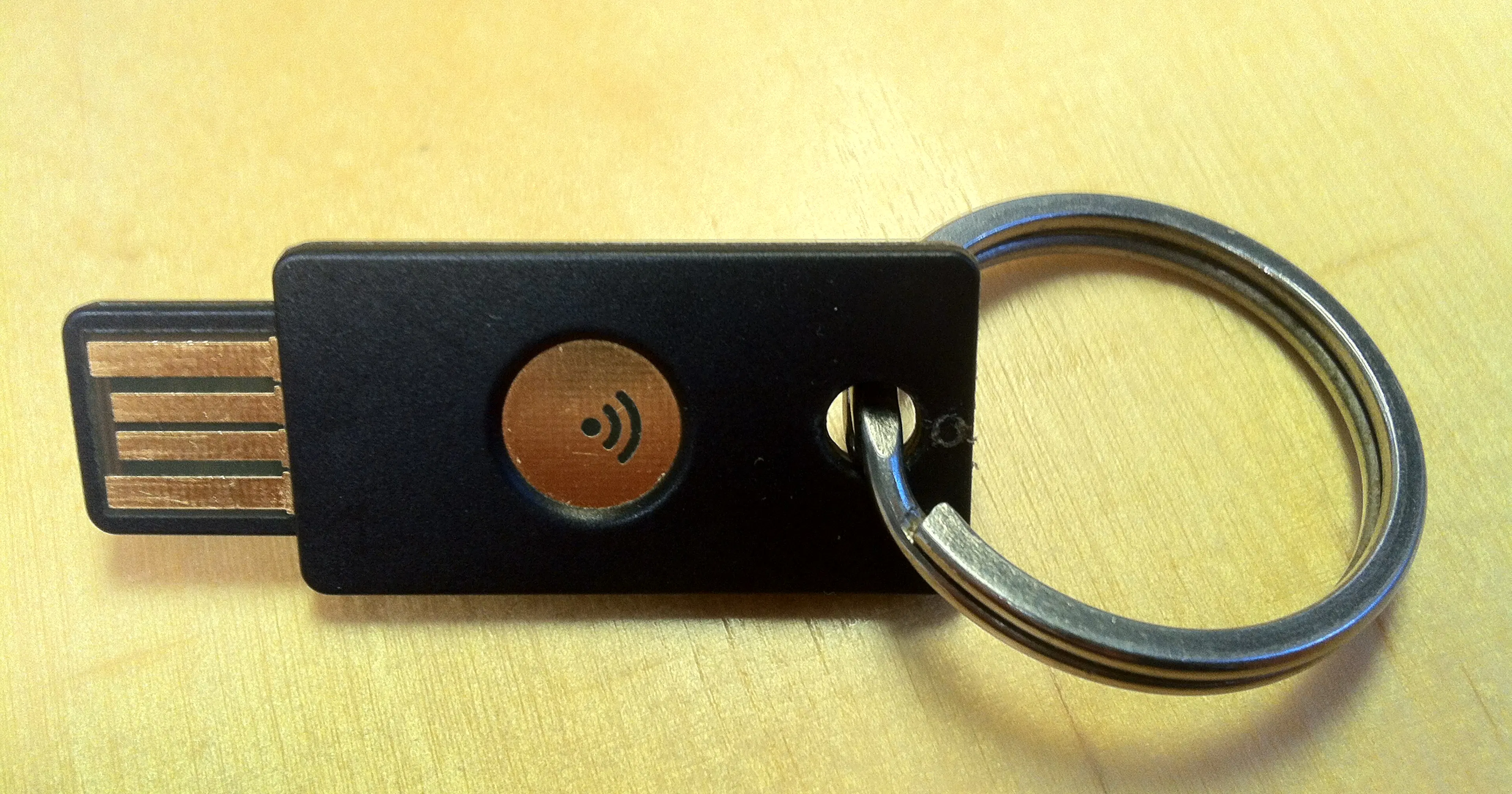 Black USB security key attached to a metal key ring on a yellow wooden surface