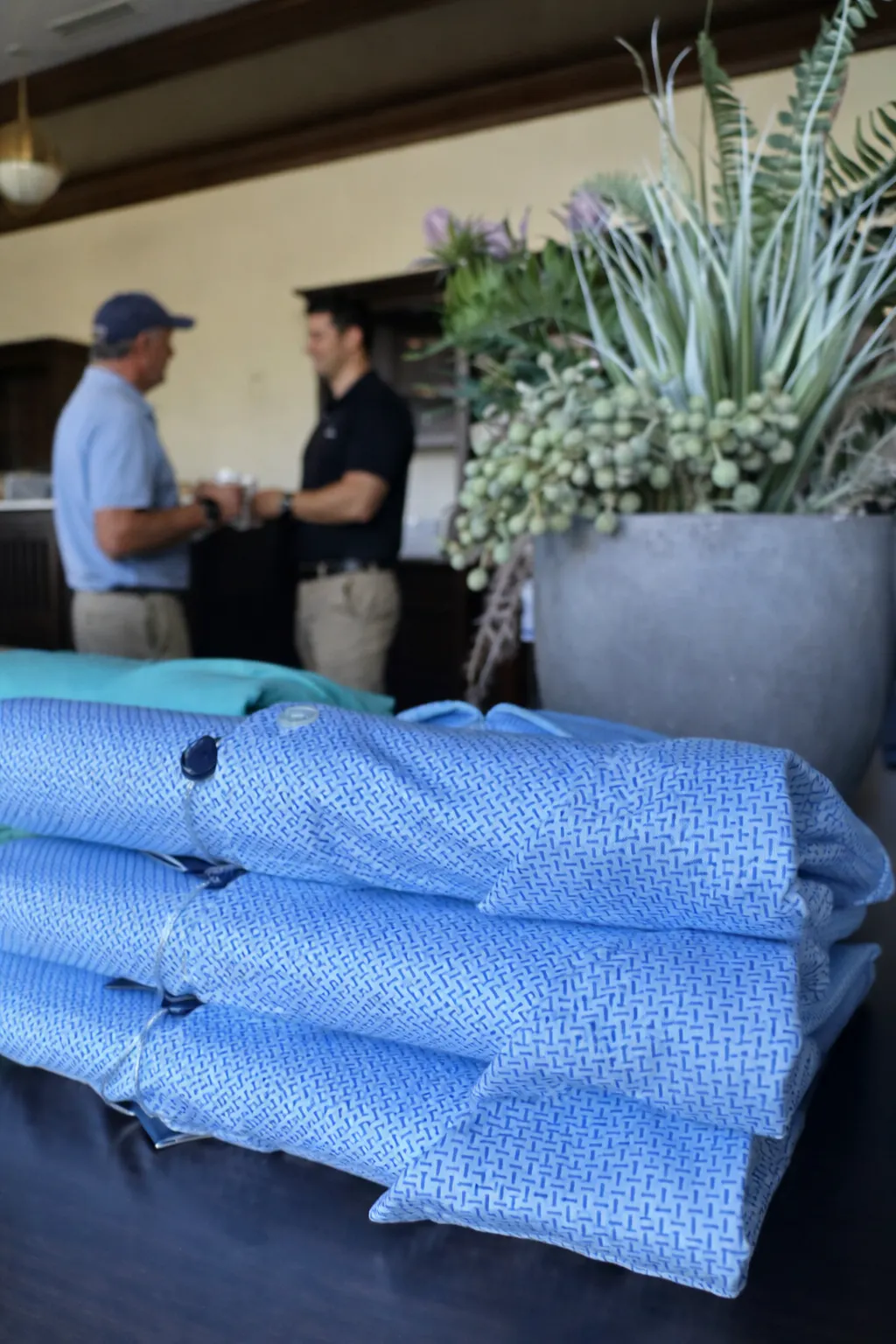 Neatly folder merchandise in the foreground with West Golf Group retail consultant reviewing pro shop layout and product presentation in the background