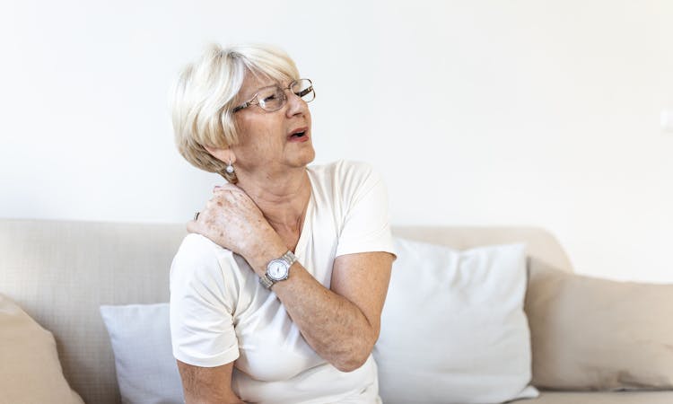 Fibromyalgie Patientin fasst sich mit schmerzverzerrtem Gesicht an den Nacken