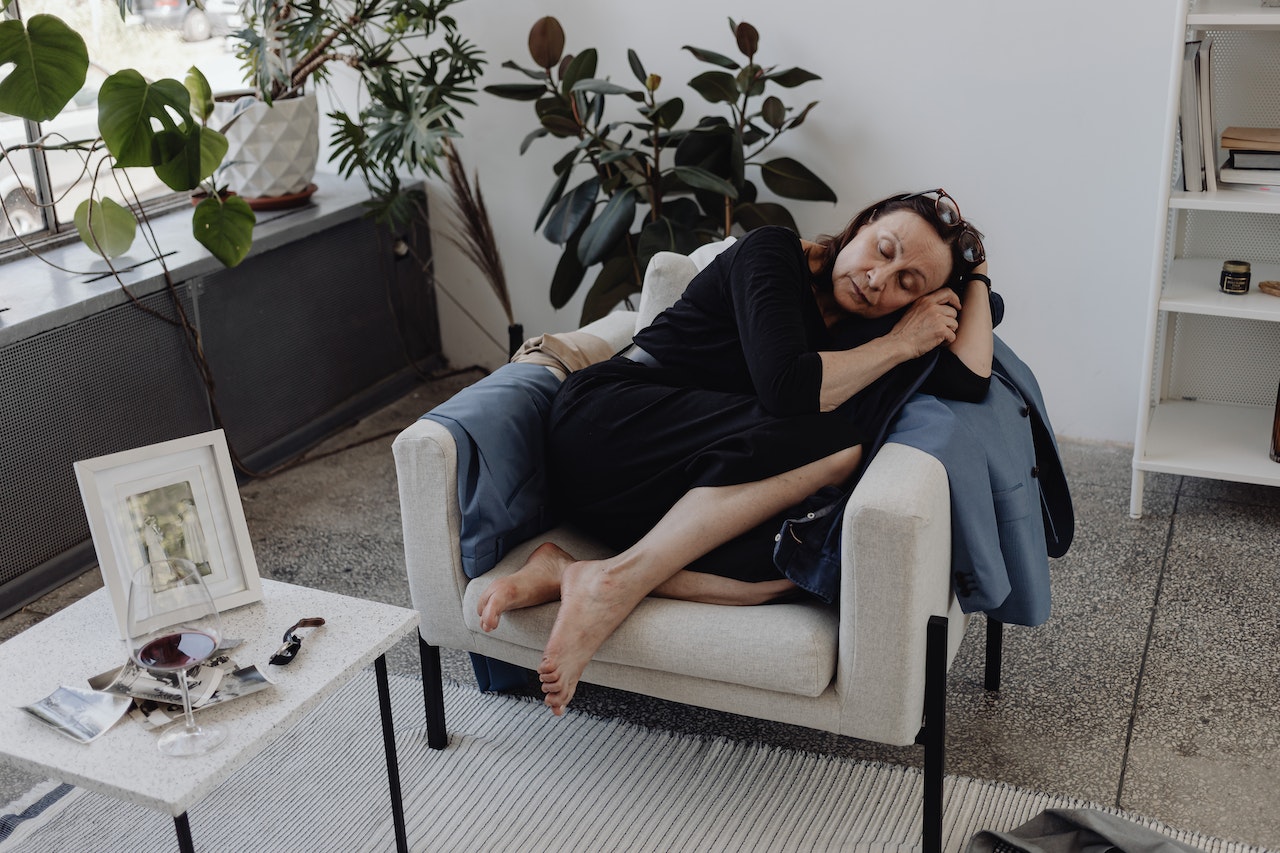 Frau schläft seitlich auf einem Sessel in einer Wohnung mit Pflanzen im Hintergrund