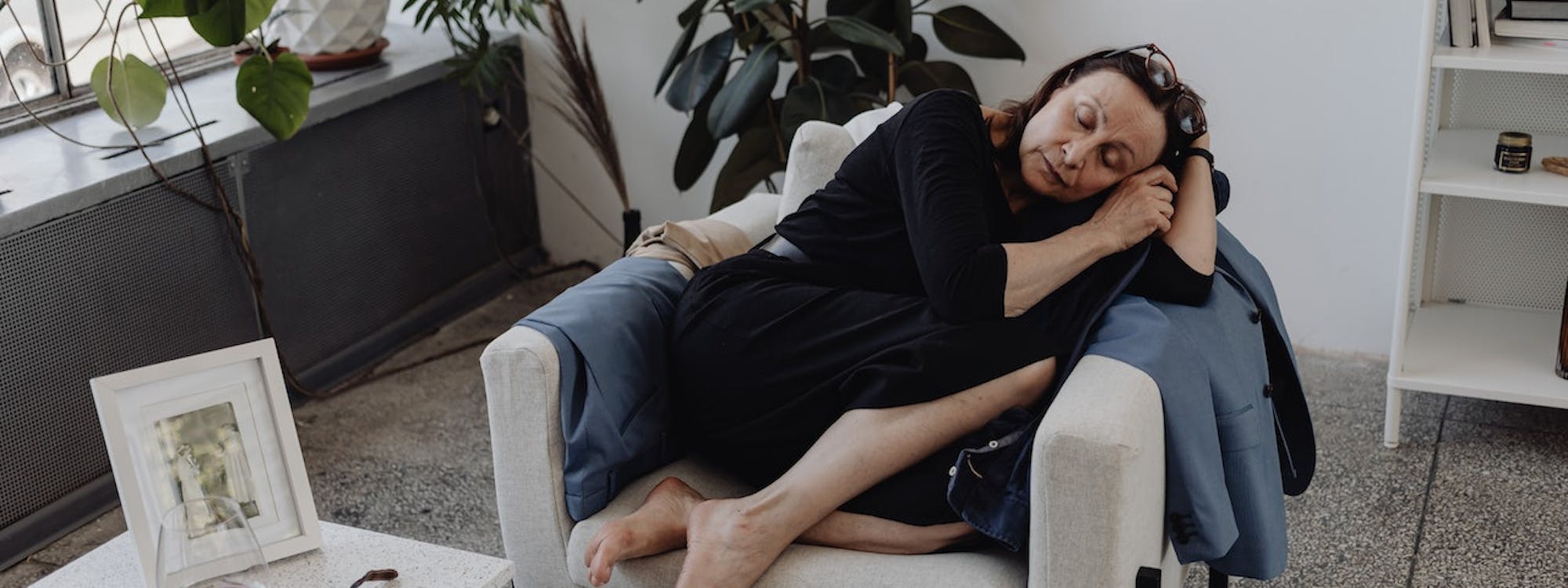 Frau schläft seitlich auf einem Sessel in einer Wohnung mit Pflanzen im Hintergrund