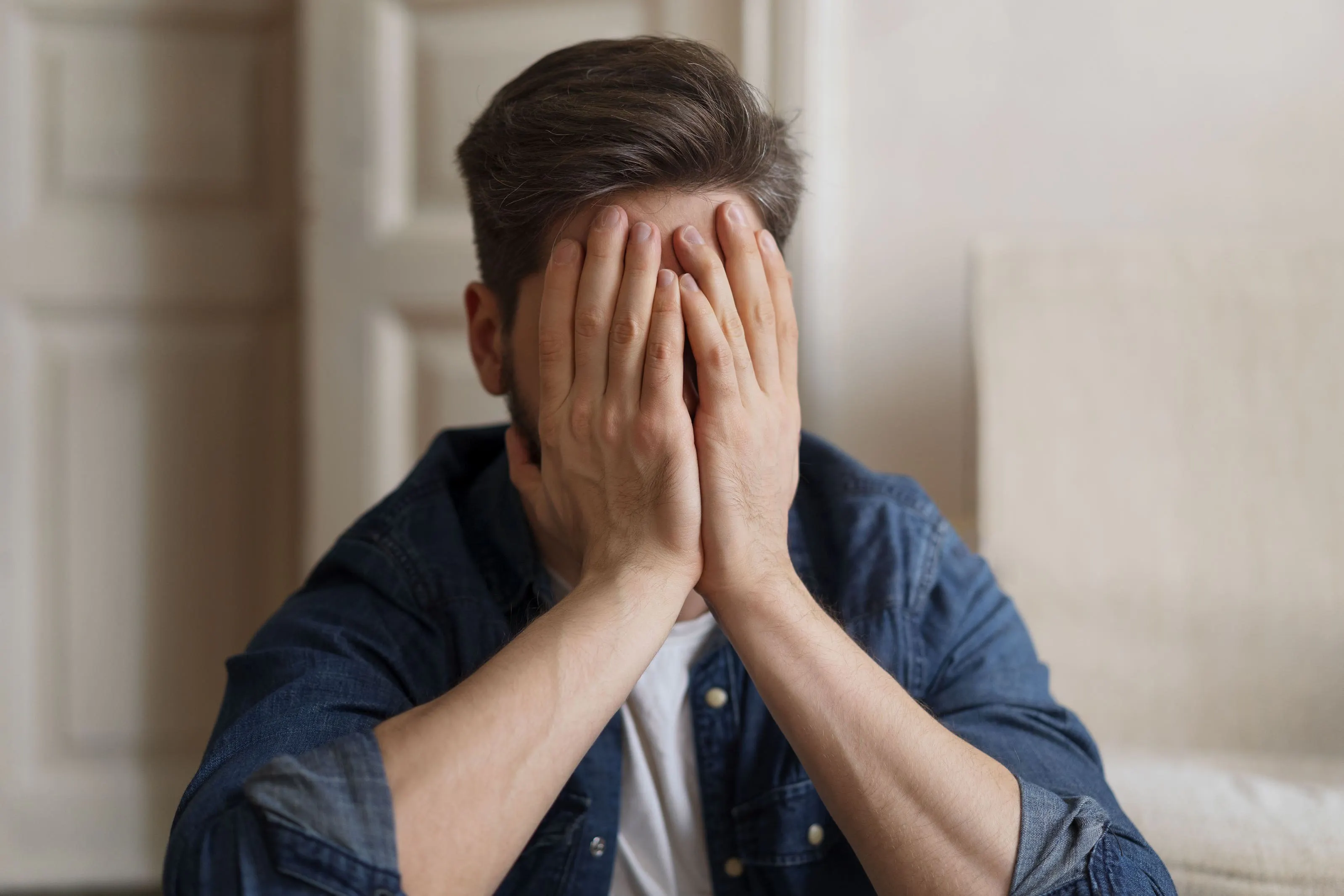 Junger Mann verdeckt sein Gesicht mit seinen Händen