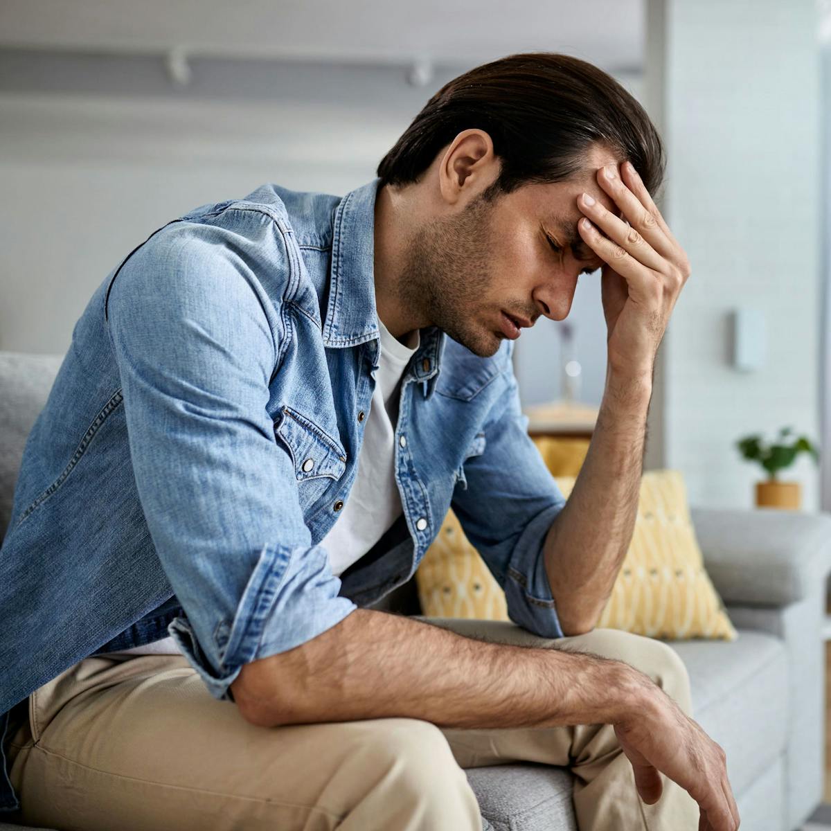 Mann mit Kopfschmerzen sitzt auf dem Sofa und fasst sich an den Kopf
