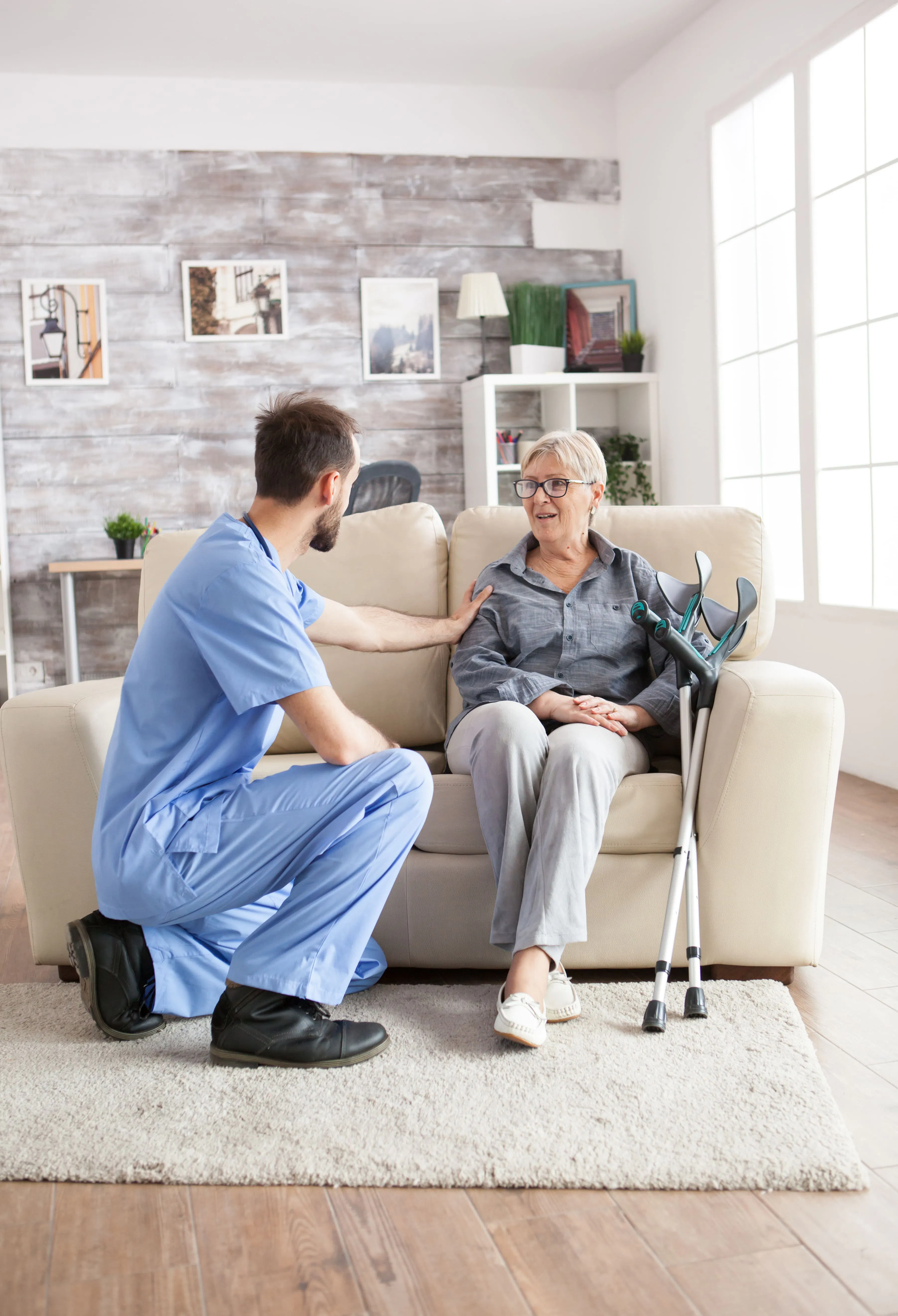 Krankenpfleger und Patientin mit Krücken sitzen auf dem Sofa