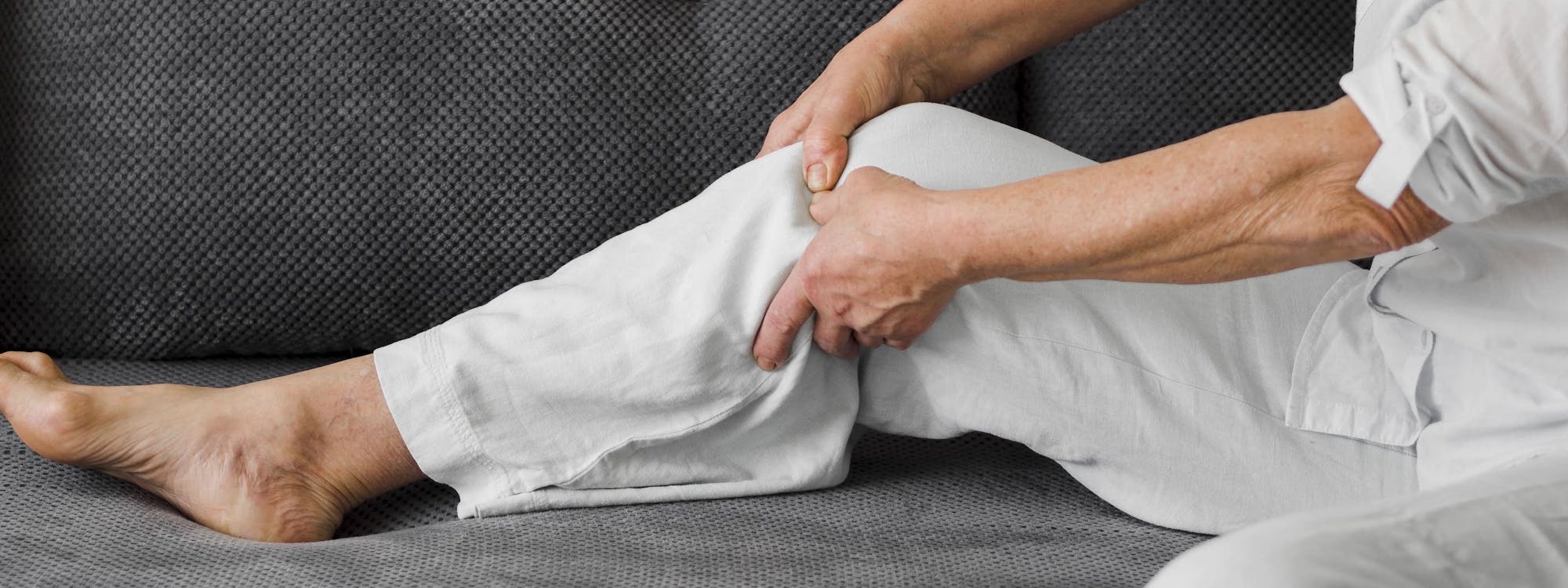 Person sitzt auf dem Sofa und fasst sich an das aufgestellte Bein