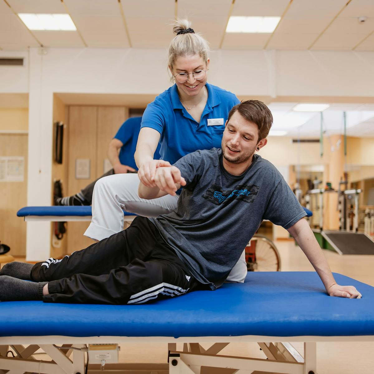 Patient auf einer Liege wird bei Übung von Physiotherapeutin unterstützt