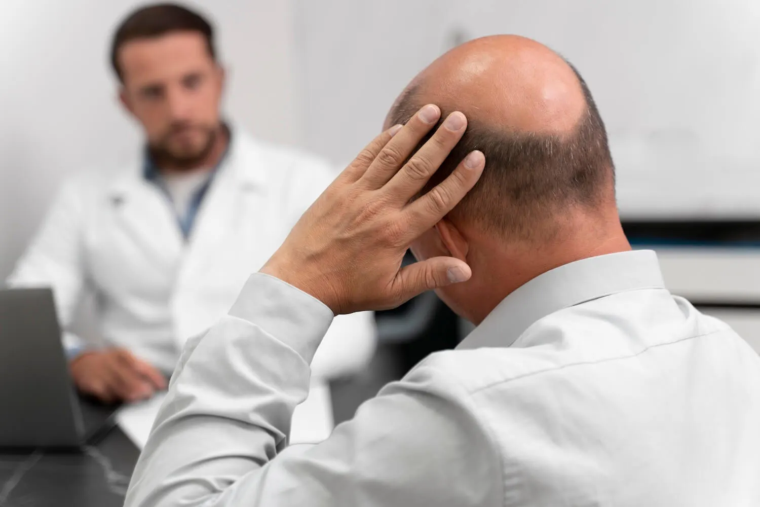 Männlicher Patient fasst sich an den Kopf während er mit einem Arzt spricht