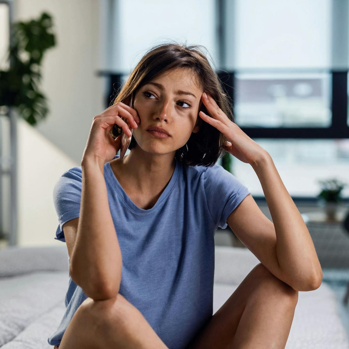 Frau mit Angststörung sitzt auf dem Fußboden und telefoniert