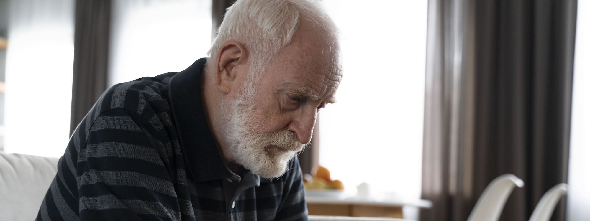 Älterer Mann sitzt im Zimmer und schaut traurig Richtung Boden