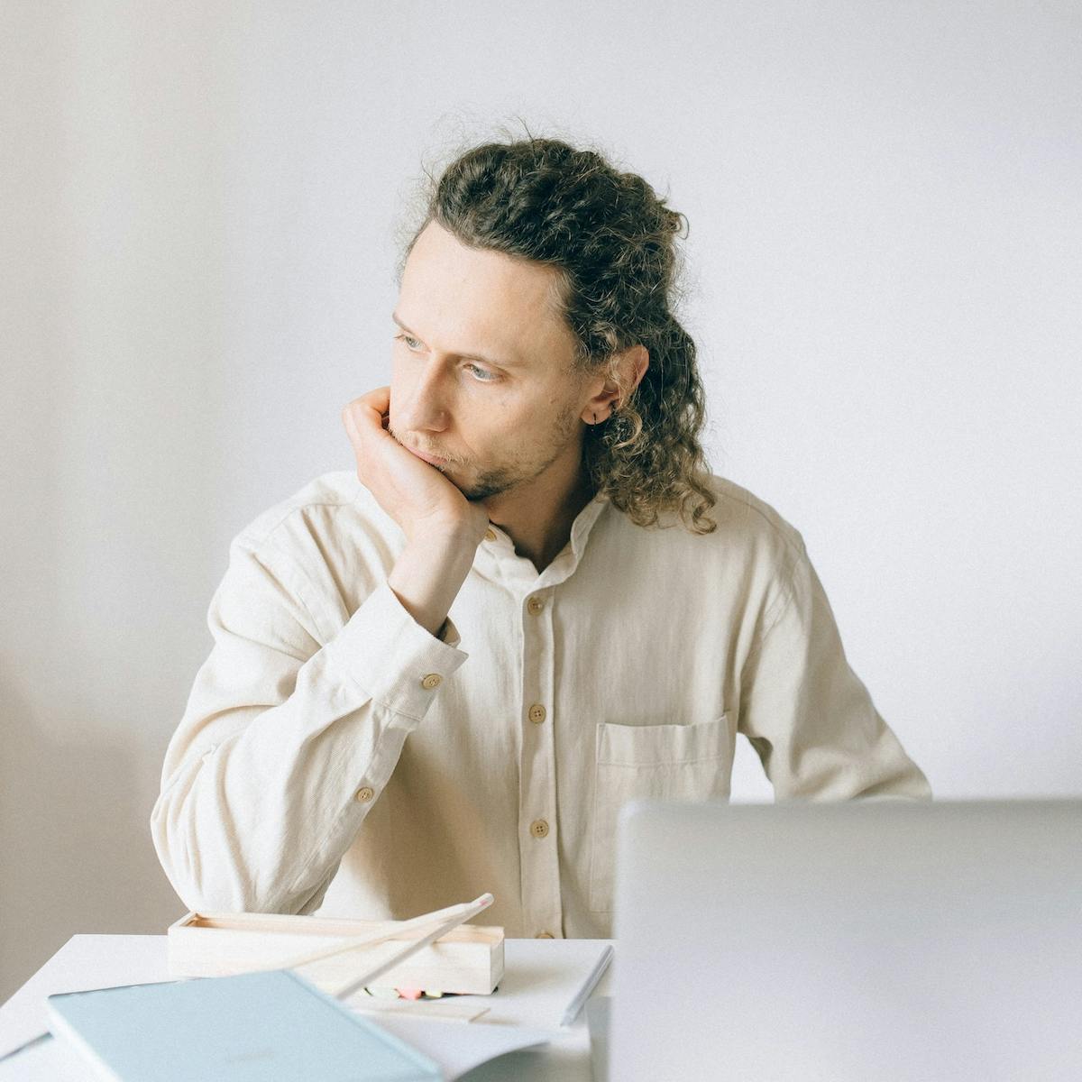 Mann sitzt erschöpft vor seinem Laptop und stützt sein Kinn auf die Hand