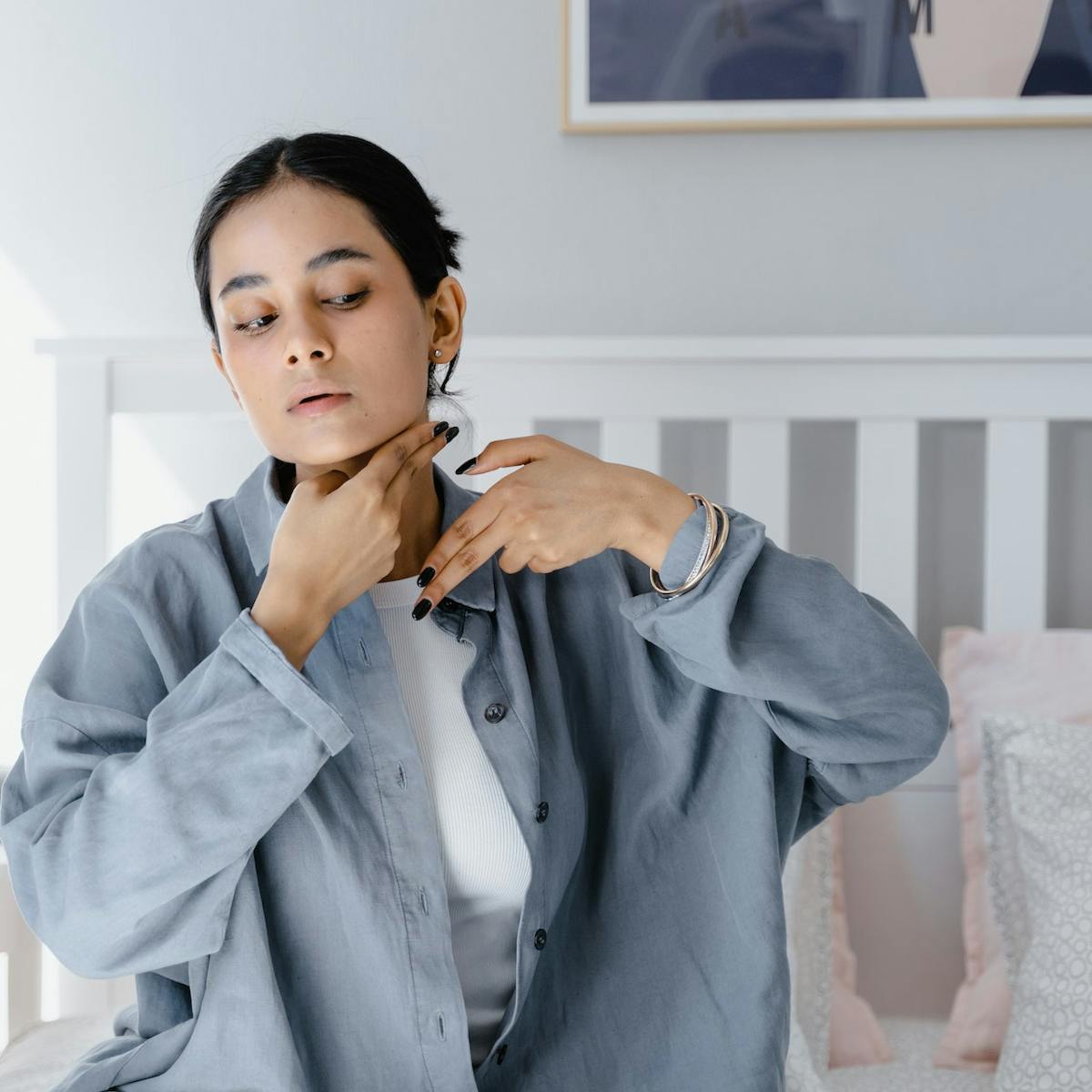 Junge Frau sitzt auf dem Bett und tastet ihren Lymphknoten am Hals ab