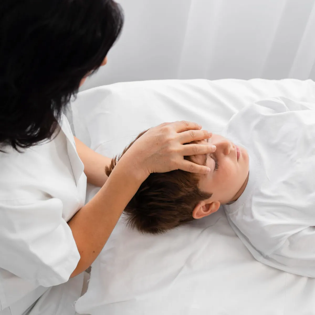 Ärztin legt die Hand auf den Kopf eines liegenden Jungen und untersucht ihn
