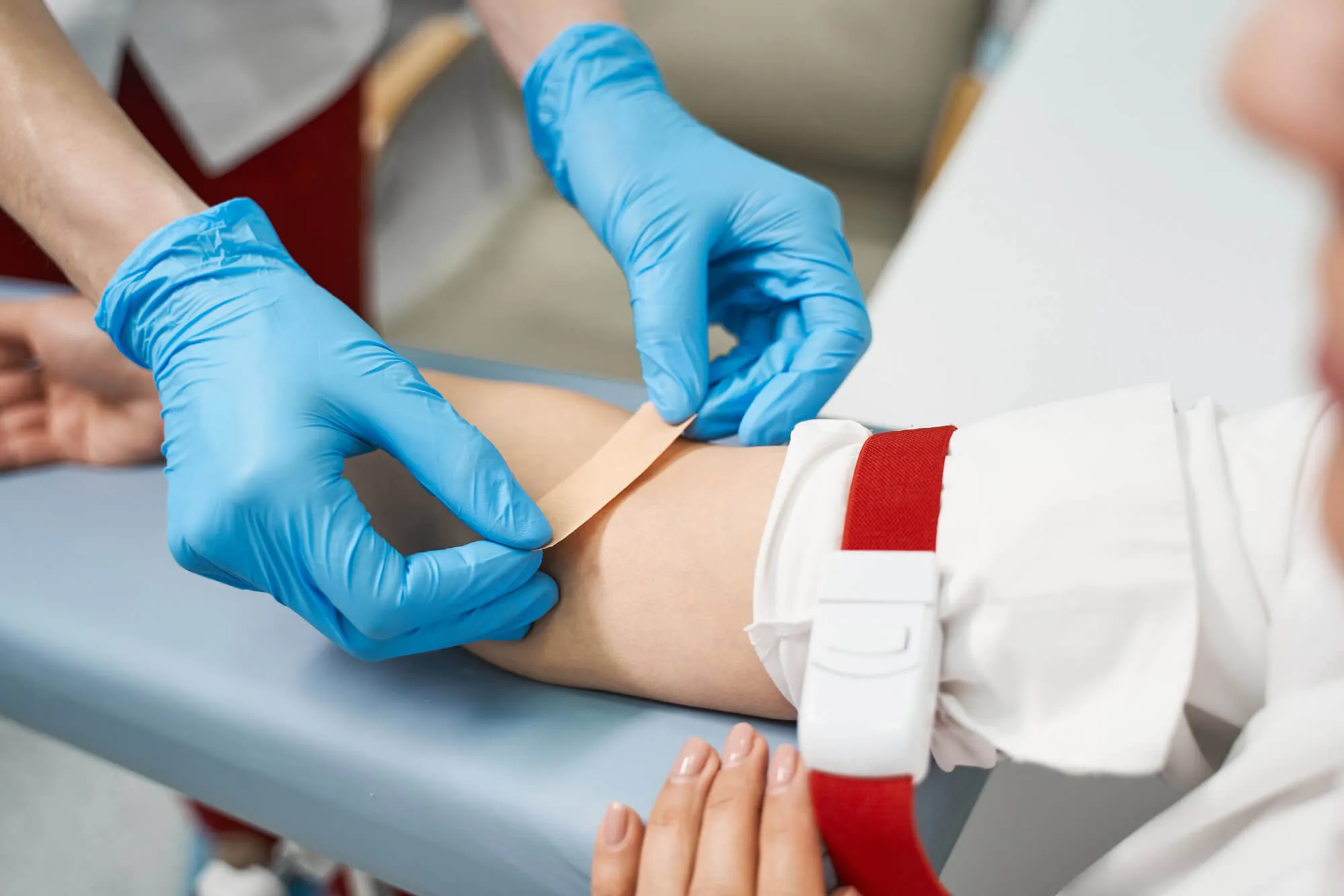 Person klebt Pflaster auf Arm einer Patientin nach Blutabnahme