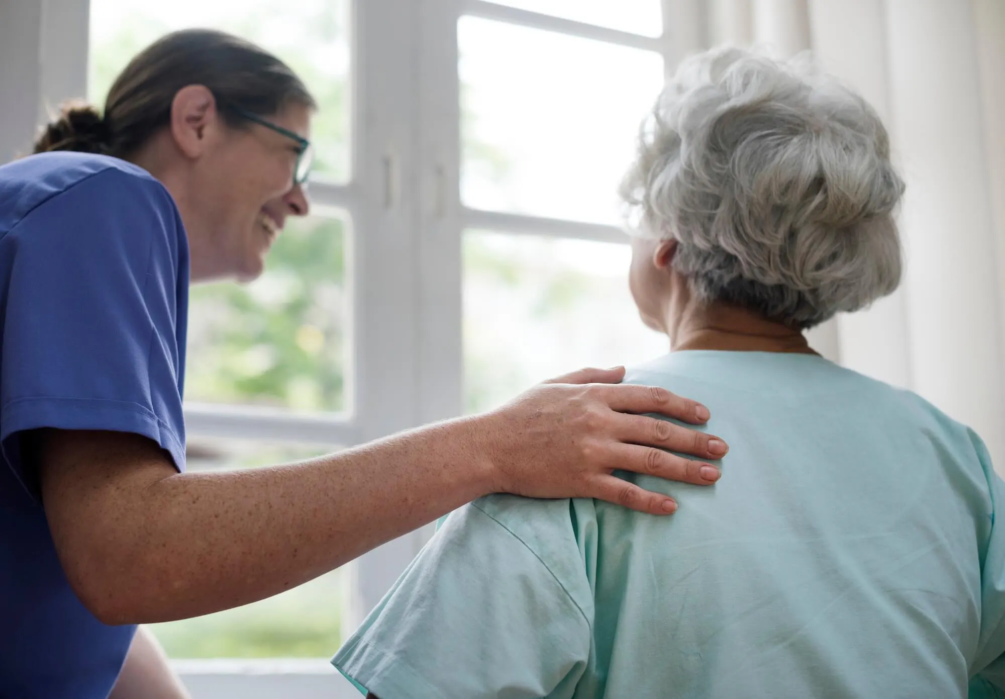 Pflegerin fasst älteren Parkinson Patientin auf die Schulter