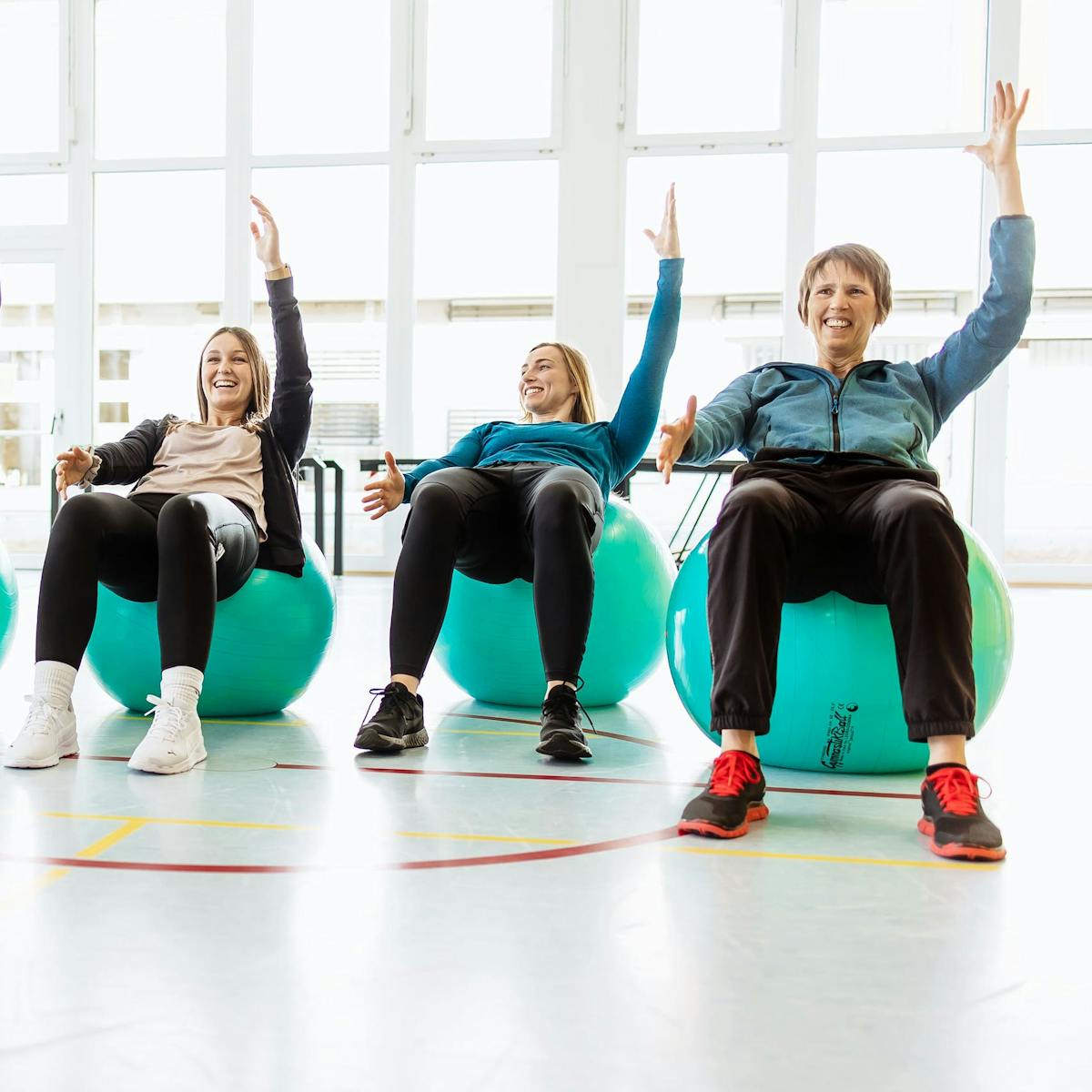 Drei Patientinnen machen nebeneinander eine Übungen auf einem Gymnastikball