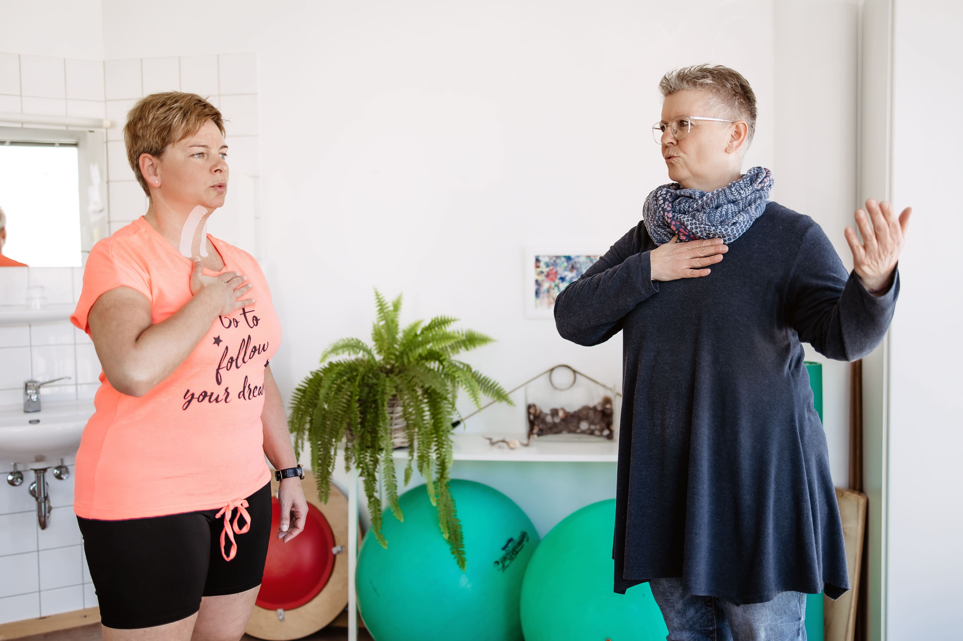 Patientin und Logopädin halten jeweils die Hand auf die Brust 