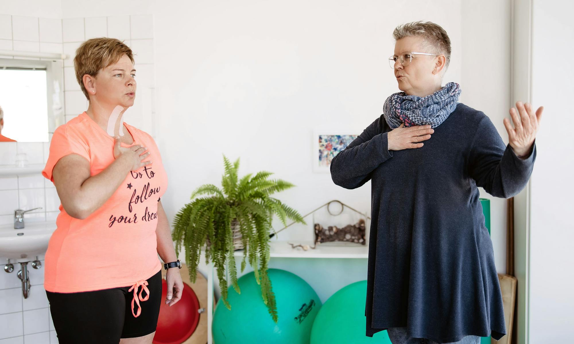 Patientin und Logopädin halten jeweils die Hand auf die Brust