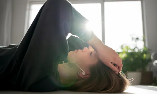 Frau liegt traurig auf dem Boden während hinter ihr die Sonne durchs Fenster scheint