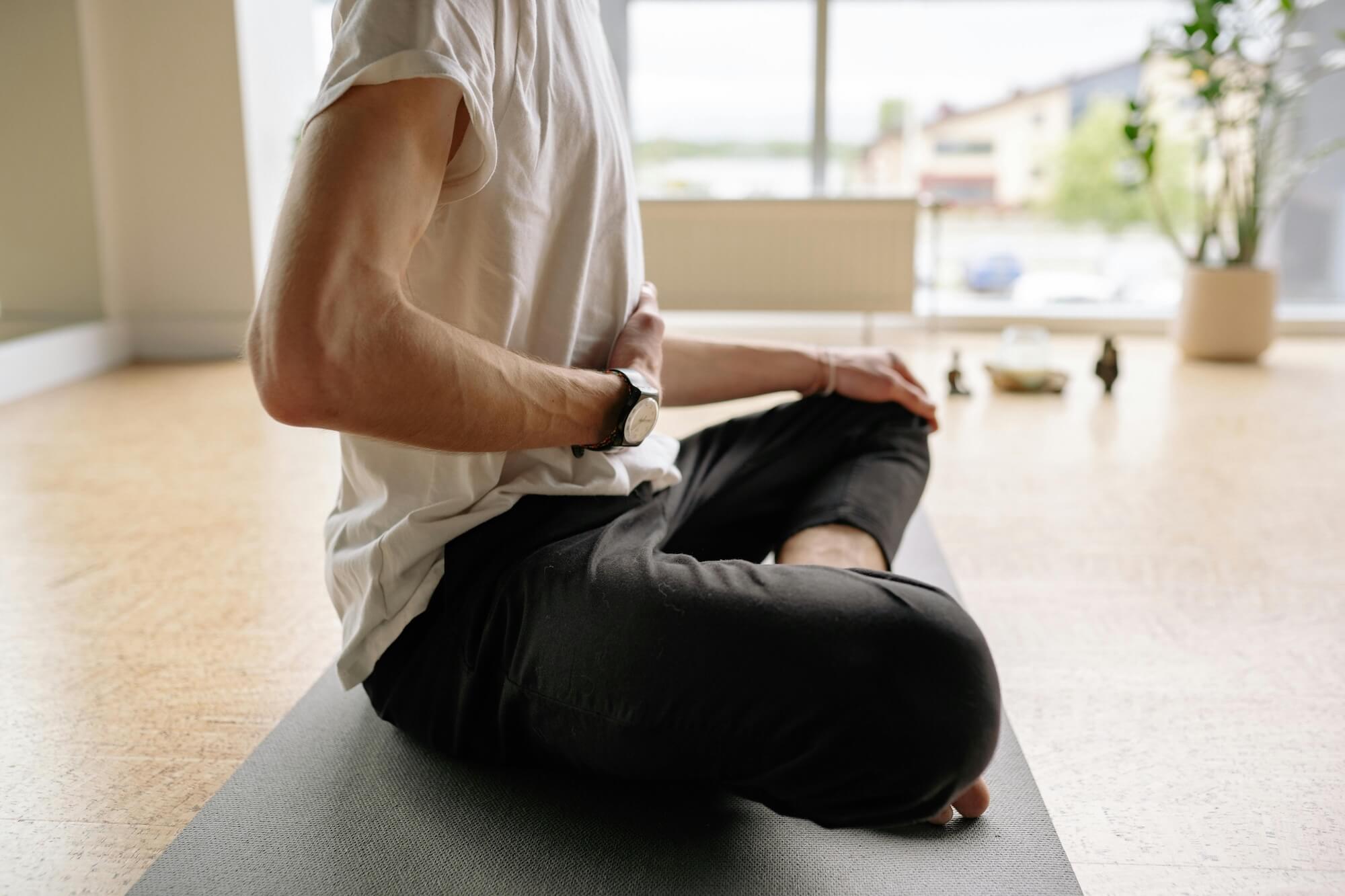 Mann im Schneidersitz macht Atemübung mit Hand auf dem Bauch