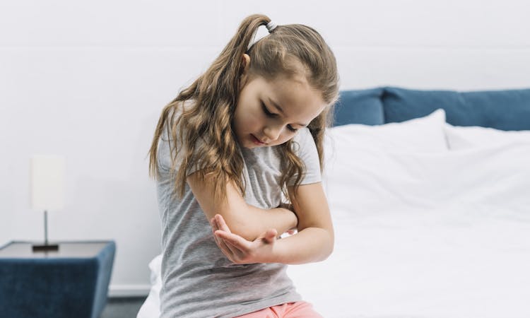 Mädchen mit Kinderrheuma fasst sich an Ellenbogen