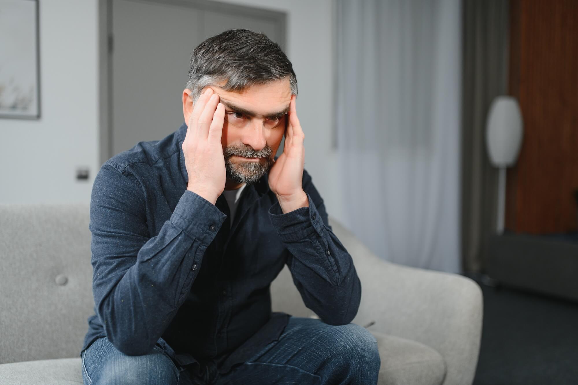 Mann sitzt auf dem Sofa und fasst sich an den Kopf