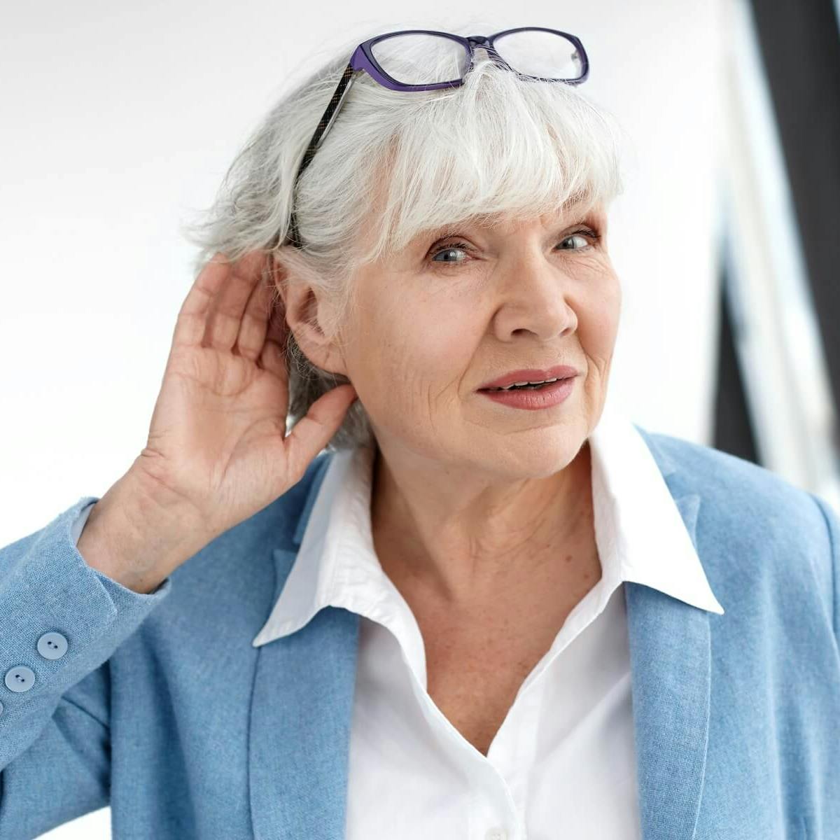 Ältere Frau mit Tinnitus hält ihre Hand hinters Ohr