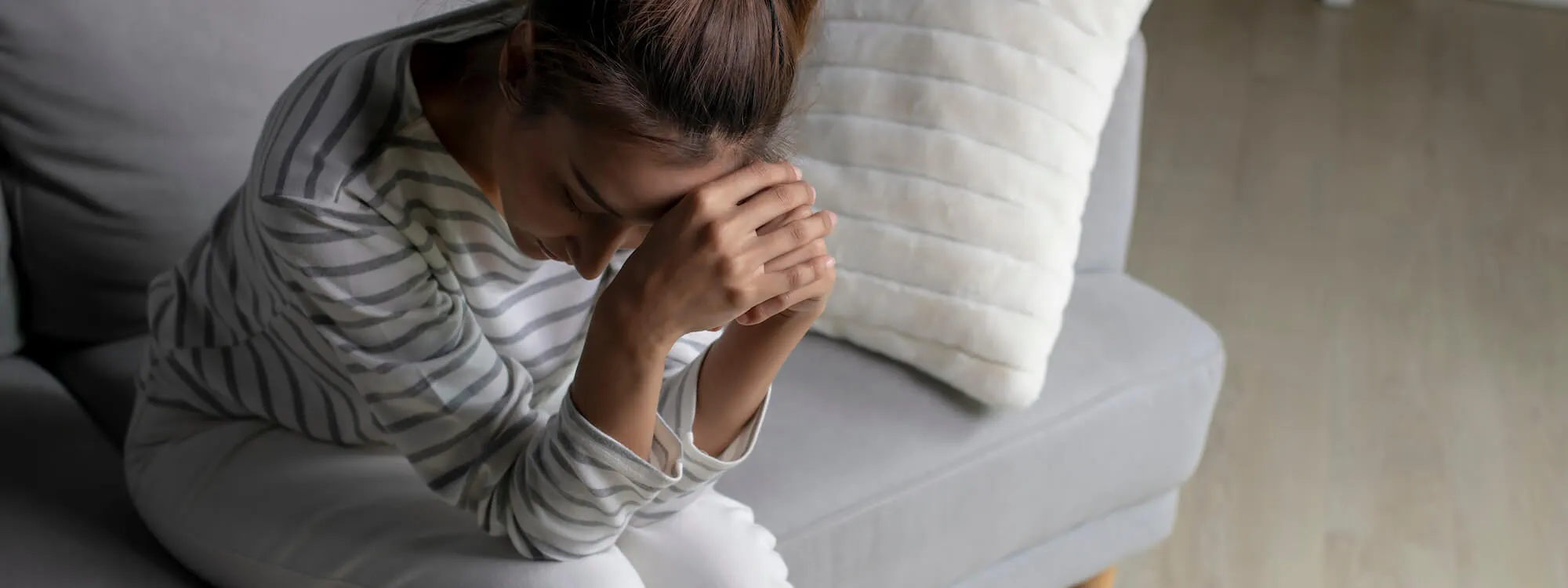 Frau sitzt besorgt auf dem Sofa und stützt ihr Gesicht gegen die Hände
