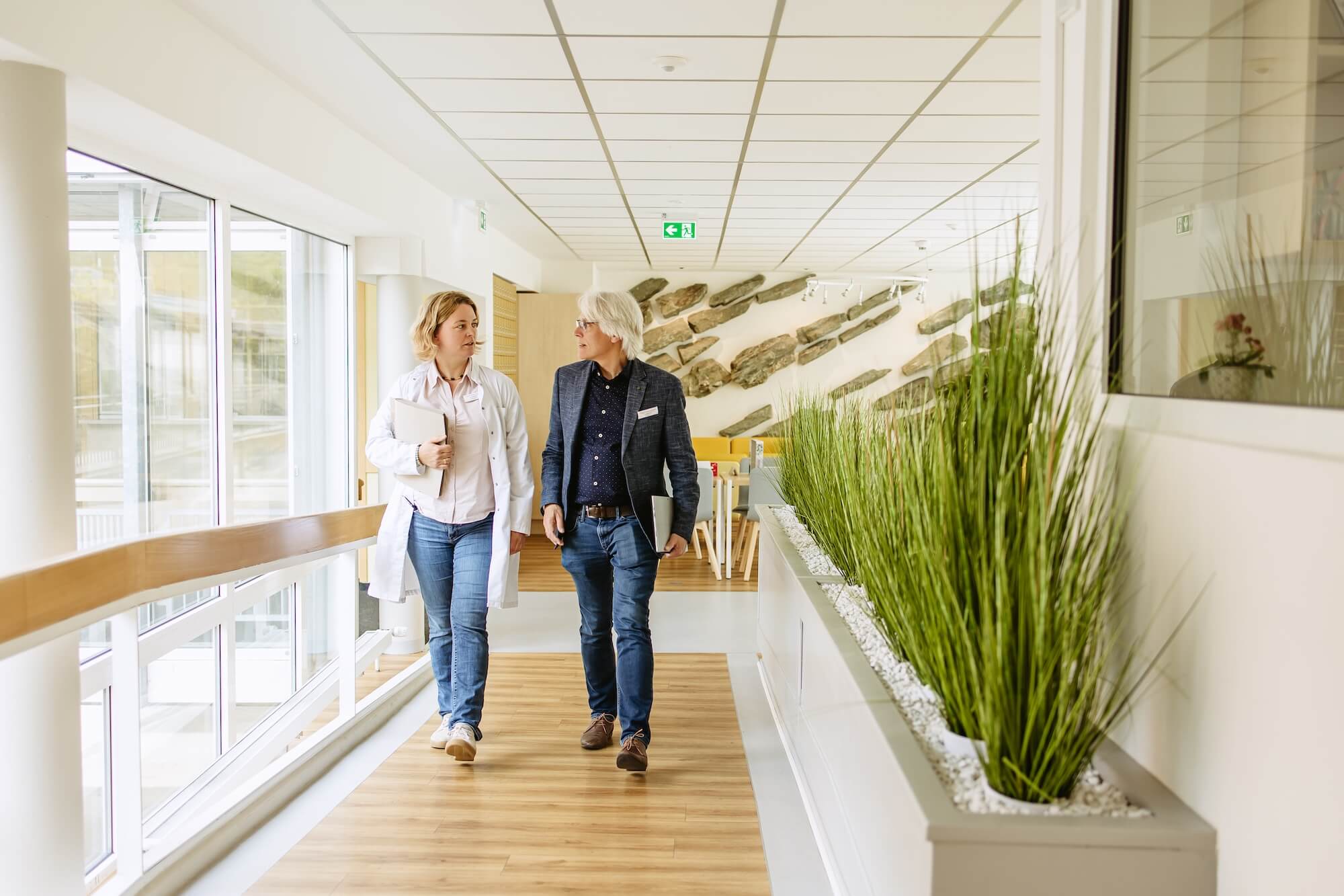 Eine Frau und ein Mann laufen durch den Flur einer Klinik