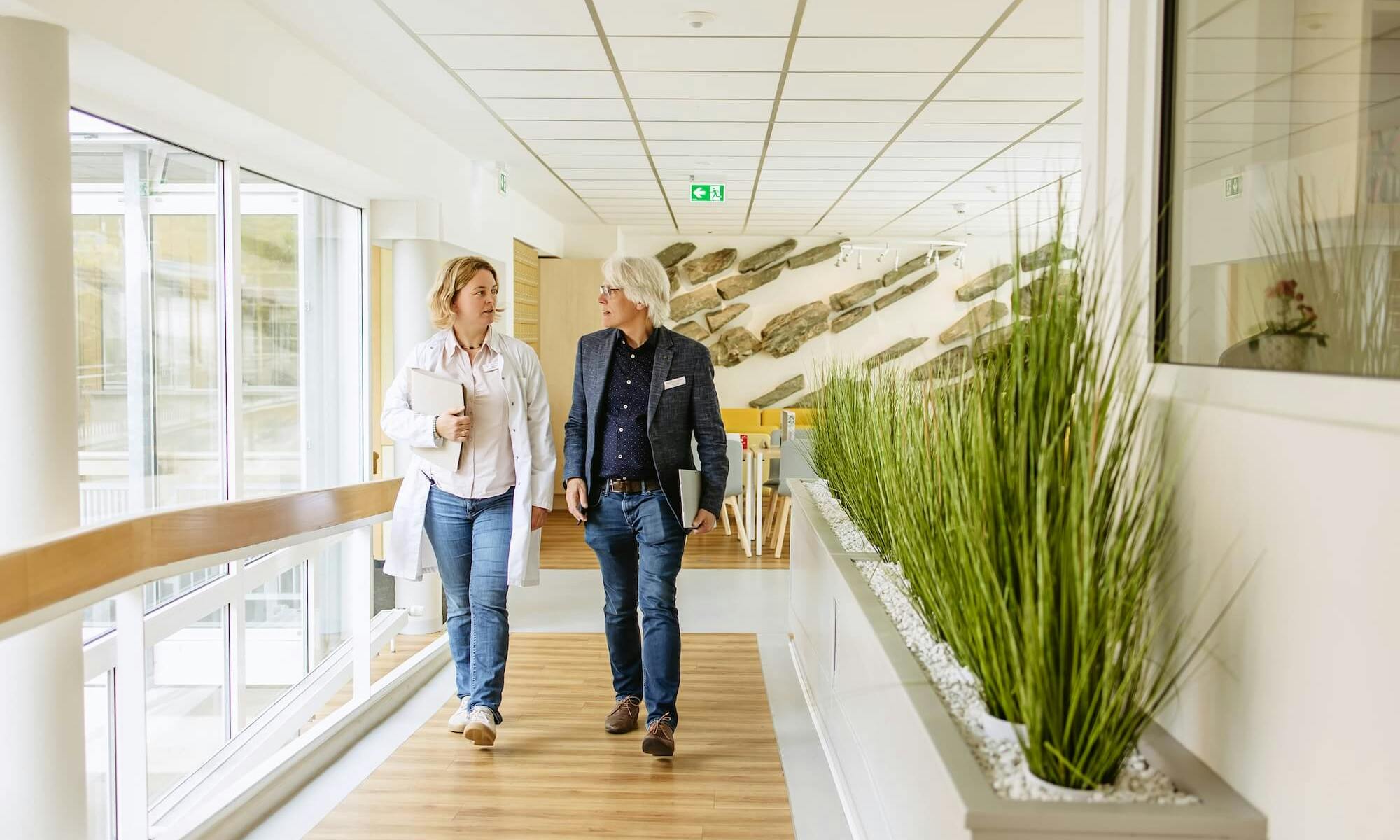 Eine Frau und ein Mann laufen durch den Flur einer Klinik